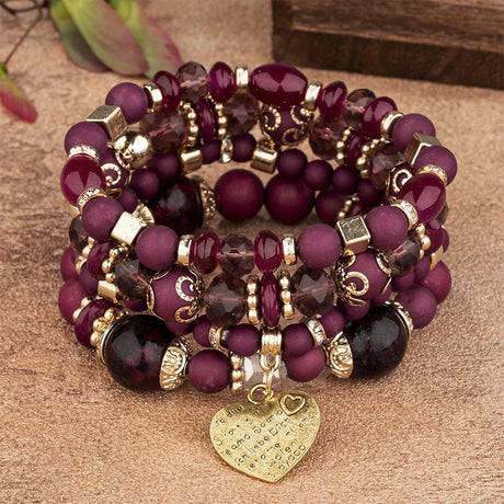Stack of purple beaded bracelets with gold accents and a heart charm on a brown surface.