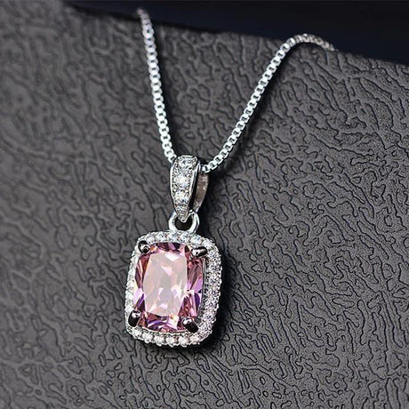 Pink gemstone pendant with silver chain on a textured gray background