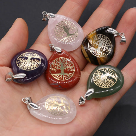 Hand holding multiple tree-of-life pendants in various colors on a dark background
