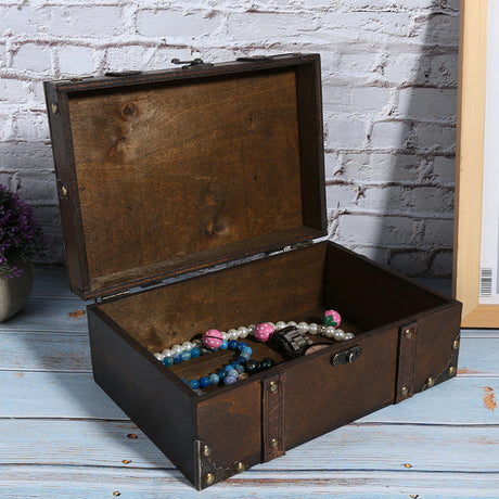 Open wooden treasure chest with jewelry on a wooden floor against a white brick wall.