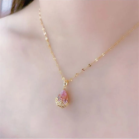Gold necklace with a pink teardrop pendant on a soft pink background