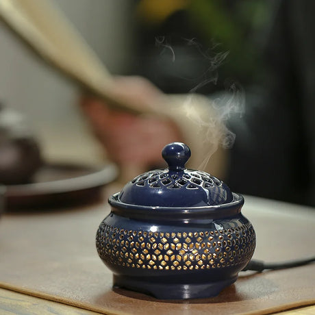 Blue incense burner with gold patterns on a wooden surface, emitting smoke.