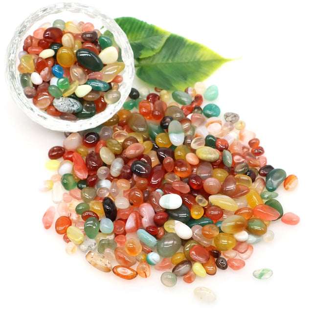 Colorful stones in a glass bowl with a green leaf on a white background
