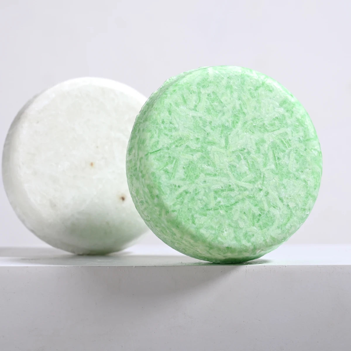 Two bath bombs, one white and one green, on a light gray background