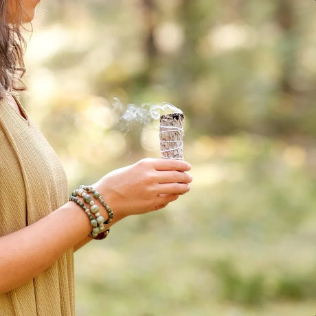 Person holding a smoking incense stick with a blurred natural background