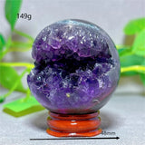 Crystal sphere with purple and clear crystals on a stand, with green leaves in the background.