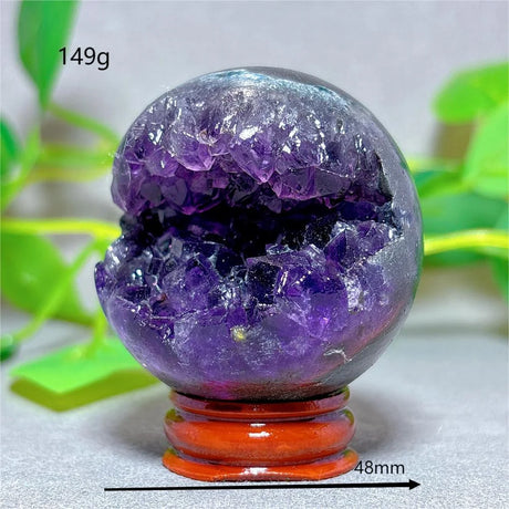 Crystal sphere with purple and clear crystals on a stand, with green leaves in the background.