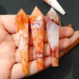 Three orange and white marbled crystal sticks held in a hand against a dark background