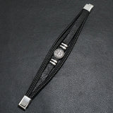 Black leather bracelet with silver accents on a dark textured surface