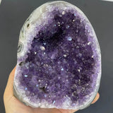 Amethyst geode held in a hand against a dark background