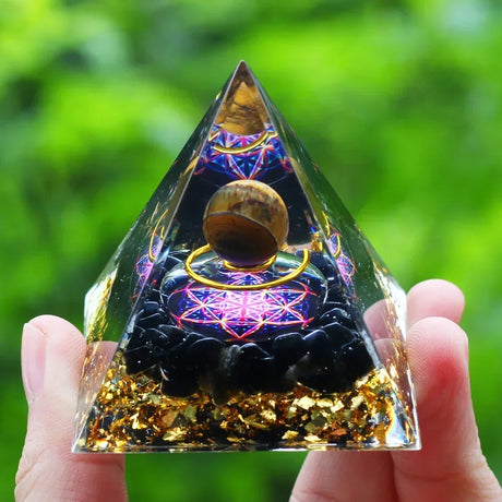 Pyramid-shaped crystal with intricate designs held by a hand against a green blurred background