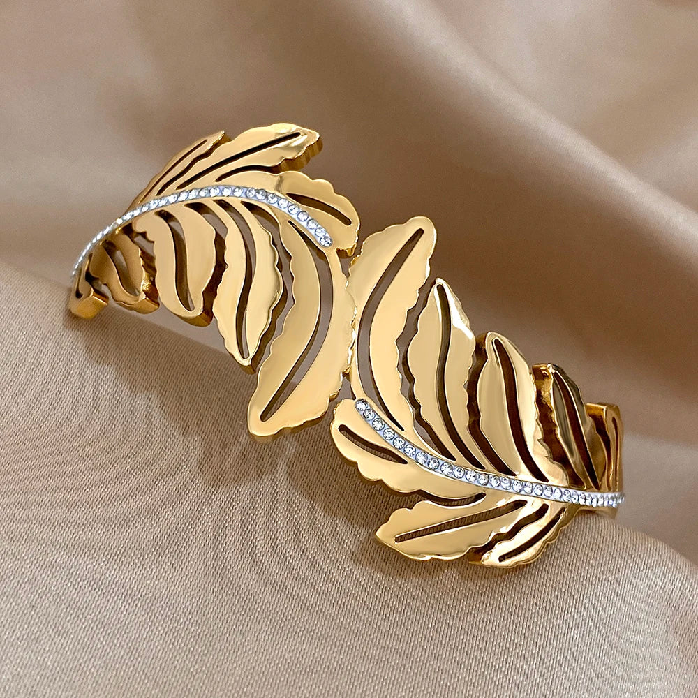 Gold leaf-shaped bracelet with diamond accents on a beige fabric background