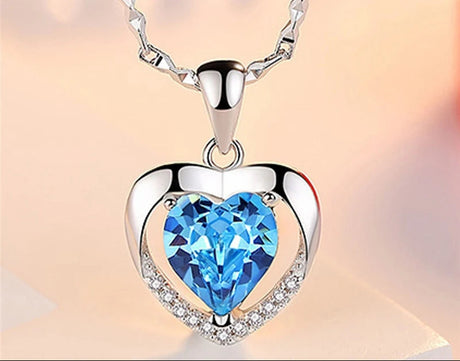 Heart-shaped necklace with blue gem and silver chain on a soft background, featuring the brand 'Giemi'.