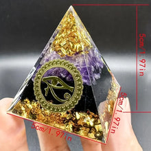 Pyramid-shaped crystal with gold leaf and amethyst, held by a hand, against a dark background.