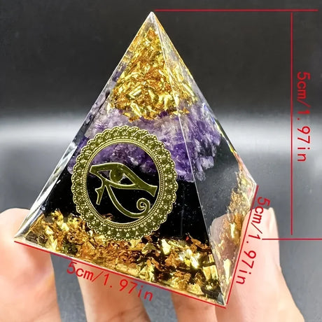 Pyramid-shaped crystal with gold leaf and amethyst, held by a hand, against a dark background.