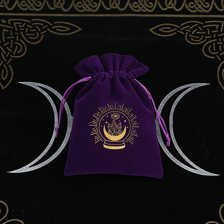 Purple velvet drawstring bag with gold emblem on a black background with white crescent moons.