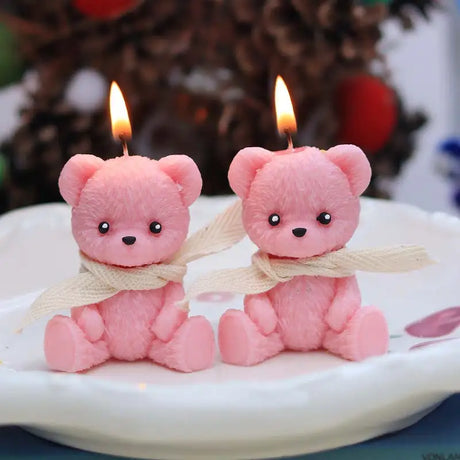 Two pink teddy bear-shaped candles with lit wicks on a white plate.