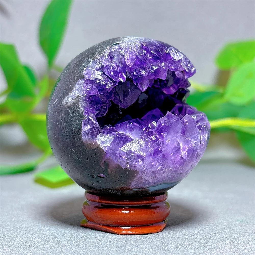 Amethyst crystal sphere on a wooden stand with green leaves in the background