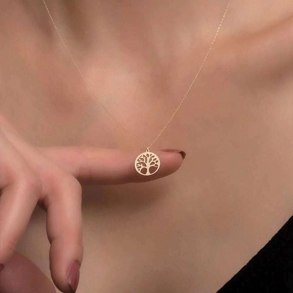 Gold necklace with a tree pendant held by a hand against a neutral background