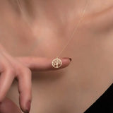 Gold necklace with a tree pendant held by a hand against a neutral background