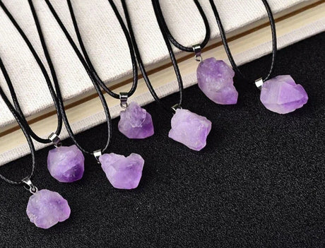 Purple crystal necklaces on black cords with a book in the background, branded 'AierCrystal'.