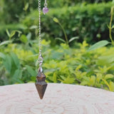 Pendulum with a purple bead on a green leafy background