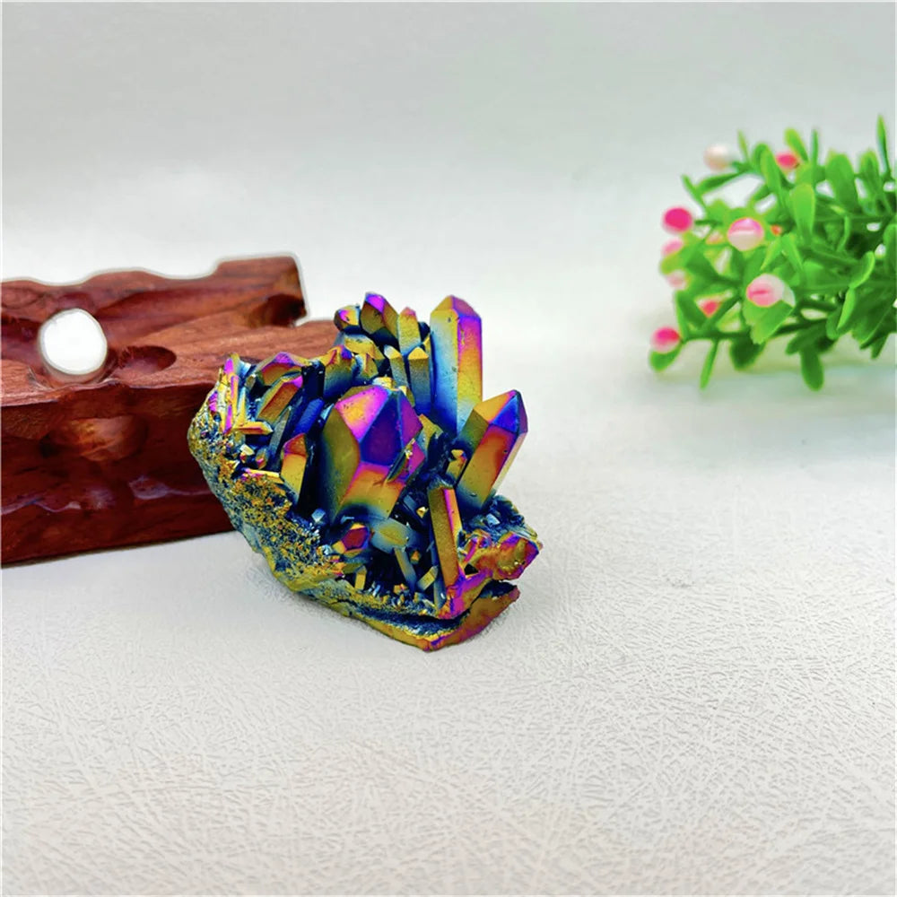 Multicolored crystal formation on a white surface with a wooden block and green plant in the background.