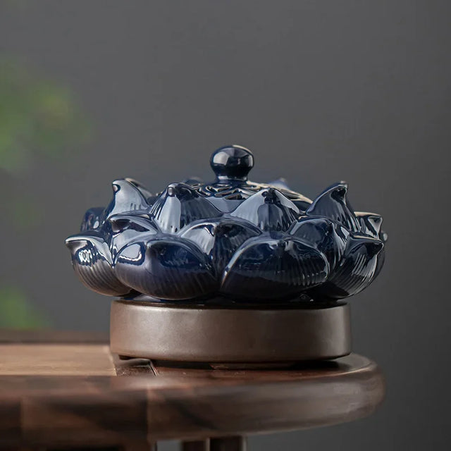 Blue ceramic incense burner shaped like a lotus flower on a wooden surface with a dark background