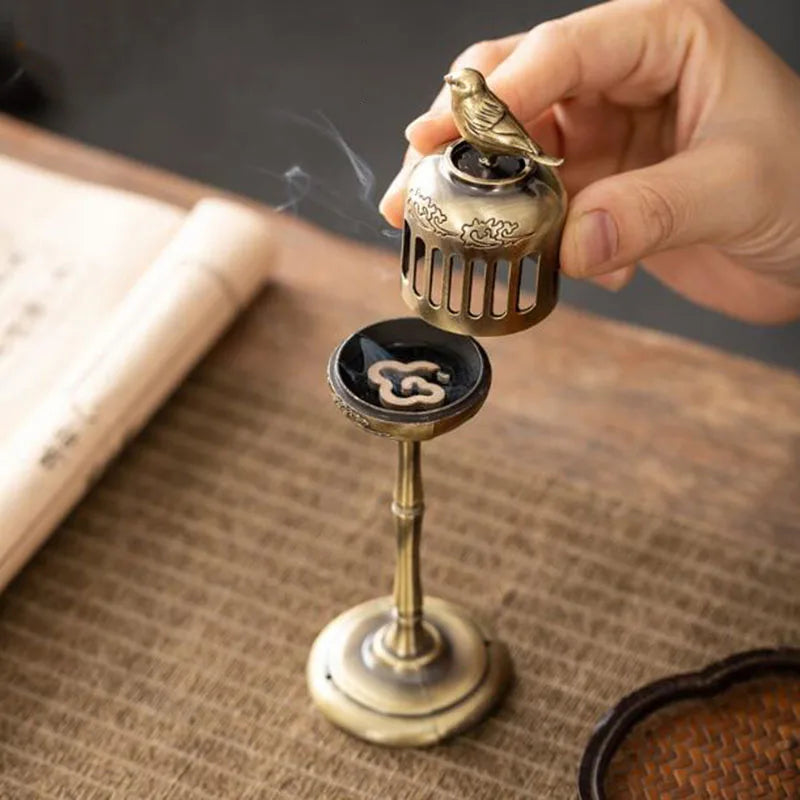 Small bronze incense burner with a bird design held by a hand on a textured surface.