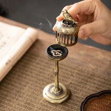 Small bronze incense burner with a bird design held by a hand on a textured surface.