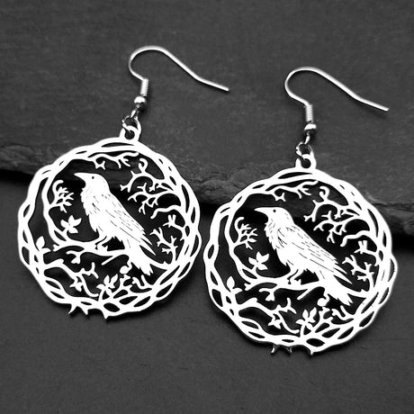 Pair of silver earrings with bird design on a dark surface
