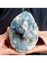 Teardrop-shaped crystal with blue and white colors held by hands against a black background