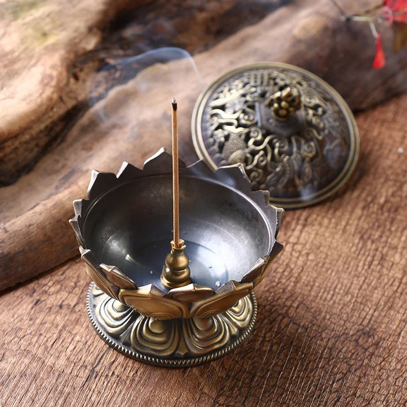 Decorative brass incense holder with a lit incense stick on a wooden surface