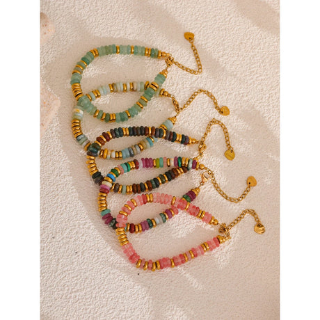 Set of colorful beaded bracelets with gold chains on a textured beige surface