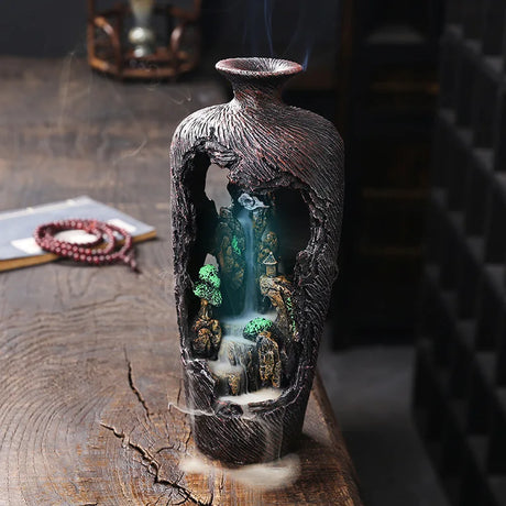 Decorative incense burner with a mountain and waterfall design on a wooden surface.