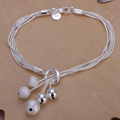 Silver bracelet with multiple strands and spherical charms on a beige background