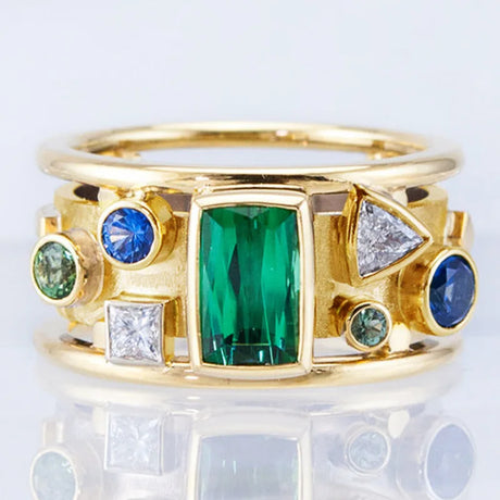 Gold ring with green and blue gemstones on a light gray background