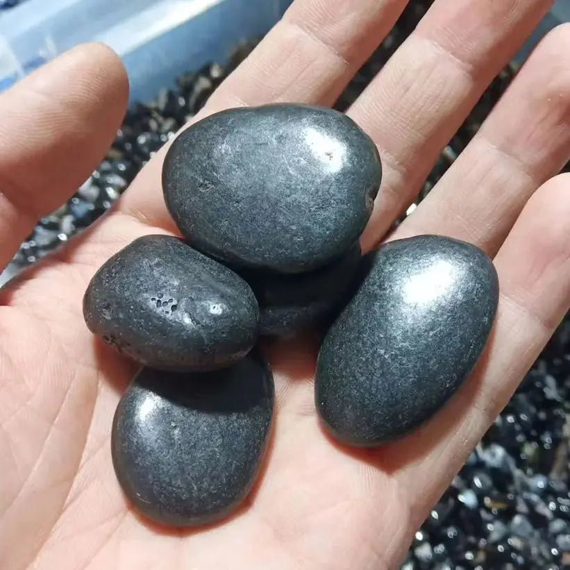 Hand holding four dark stones with a blurred natural background