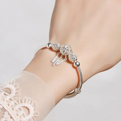 Silver bracelet with floral charms on a wrist against a light background