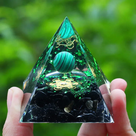 Pyramid-shaped crystal with green and black design held by a hand against a blurred green background