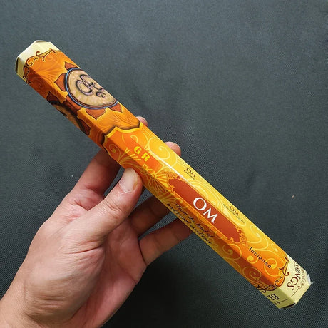 Hand holding a box of incense sticks with 'OM' text on a dark background