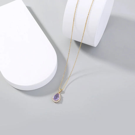 Gold necklace with a purple teardrop pendant on a white surface
