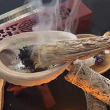 Incense stick burning in a holder with smoke rising, surrounded by various items on a dark surface.
