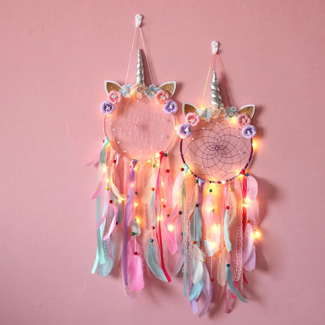 Unicorn-shaped dreamcatcher with colorful feathers and lights on a pink background