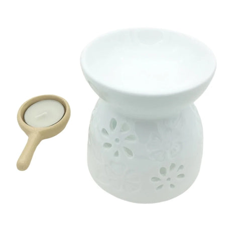 White ceramic oil burner with floral designs and a small wooden tray with a candle on a white background