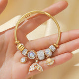 Gold bracelet with various charms held in a hand against a beige background