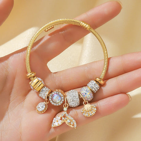 Gold bracelet with various charms held in a hand against a beige background