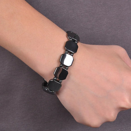 Black beaded bracelet on a wrist against a gray background
