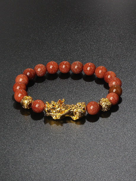 Bracelet with red beads and gold dragon charm on a dark background