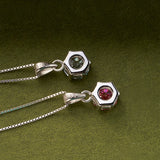 Two silver hexagonal pendants with gemstones on a green background